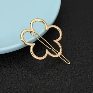 Detailed view of a golden four-leaf flower metal hair clip on a textured surface