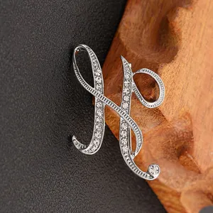 Broche letra H plateada con cristales brillantes sobre fondo de cuero oscuro