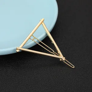 Detail of a geometric gold triangular hair clip with a wavy metal pin on leather background