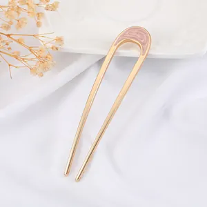 Detailed macro view of pink enamel U-shaped hair pin with elegant golden spiral pattern