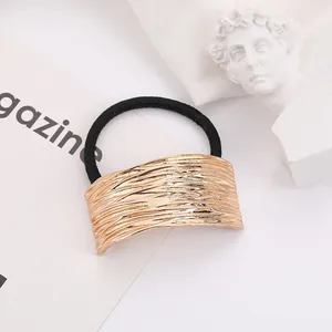 Macro detail of golden metal hair tie with brushed texture and black elastic band