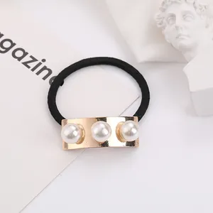 Macro detail of golden metal bar with three white pearls on a black elastic hair tie