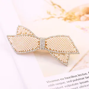 Dettaglio di elegante fermaglio a fiocco con perle bianche e strass su base dorata lucida