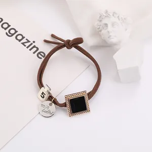Detail of brown braided hair tie with a number 5 charm and silver logo pendant