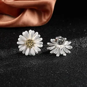 Macro detail showing front and back of small white daisy brooch with silver pin fastener
