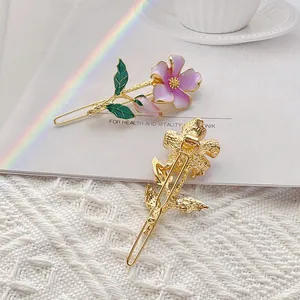 Elegant gold flower hair clip with purple enamel and green leaves on white lace background