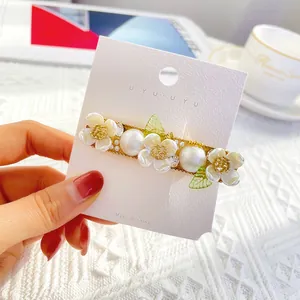 Elegante bloemen haarclip met witte bloemen, parels en groene bladeren op gouden basis