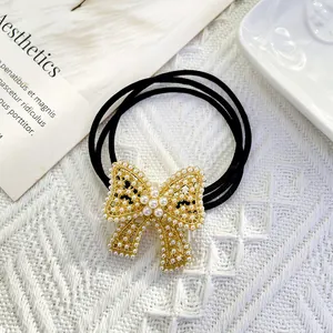 Detailed shot of a black elastic hair tie with a gold-tone pearl bow on knit texture