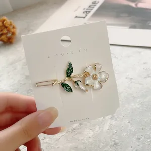 Detailed close-up of a white flower hair clip with golden edges on a display card