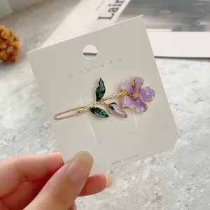 Detailed close-up of a purple enamel flower hair clip with golden metal edges and green leaf
