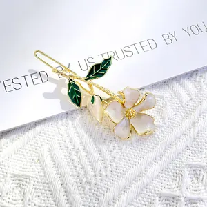Detailed macro view of an elegant floral hair clip with white petals and green enamel leaves