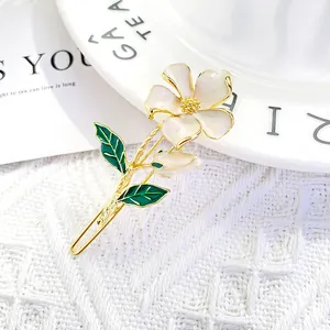 Floral hair clip with pearlescent white petals and green enamel leaves on gold base