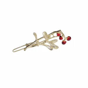 Fermaglio per capelli dorato con bacche di ciliegia rosse e foglie su fondo bianco
