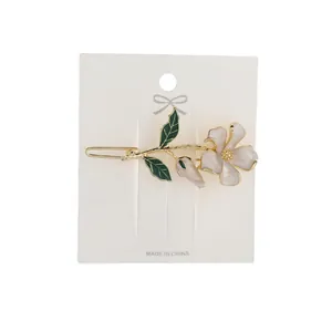 Elegant gold flower hair clip with pink enamel petals and green leaves on a display card