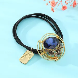 Detalle de la goma de pelo dorada con cristal azul y placa 'Handmade with Love'