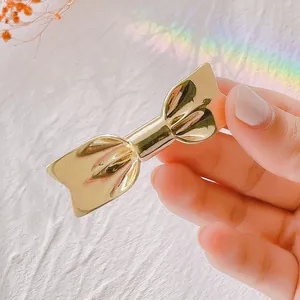 Poliertes goldene Metall-Haarschleife in der Hand mit sanften Regenbogenreflexen