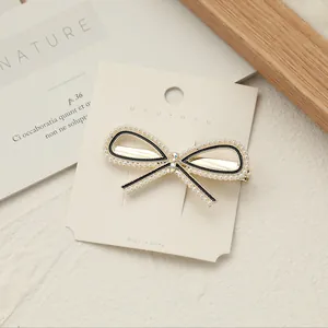 Dettaglio del fermaglio a fiocco con piccole perle, strass scintillanti e motivo a righe