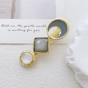 Detailed close-up of a golden alloy hair clip with grey resin and white cat-eye stone