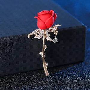 Close-up of elegant red rose brooch with gold leaves, rhinestones and a teardrop pendant