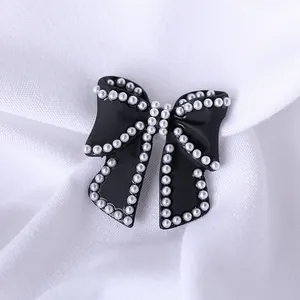 Elegant black bow brooch accessory with white imitation pearls on white fabric