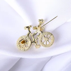 Detailed back view of a golden bicycle brooch with secure pin clasp on white silk fabric
