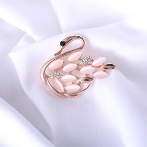Close-up of elegant rose gold swan brooch with pink stones and sparkling zircons on fabric