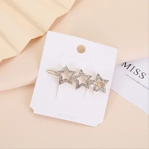 Dettaglio di un fermaglio per capelli dorato con tre stelle di strass su cartoncino