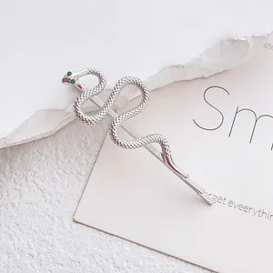 Silver snake hair clip with green gemstone eyes on minimalist textured background
