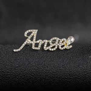 Macro detail of golden Angel letter brooch with sparkling white rhinestones and a teardrop gem