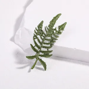 Detailed close-up of green fern leaf brooch with enamel finish on textured stone