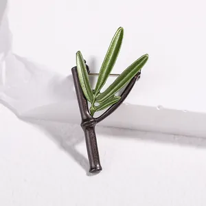 Detailed view of dark green bamboo leaf brooch with gold pin on white stone