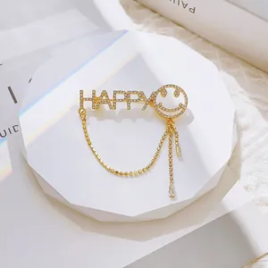 Golden HAPPY letter brooch with rhinestone smile and tassel on white display stand