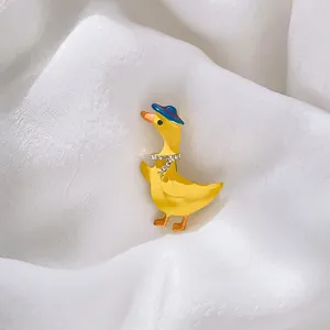 Broche canard jaune avec chapeau bleu et collier en strass sur fond de soie blanche