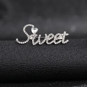 Close-up of a silver-toned 'Sweet' brooch with heart-shaped stone and crystal pavé details