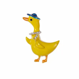Broche canard en émail jaune avec chapeau bleu et collier de strass sur fond blanc