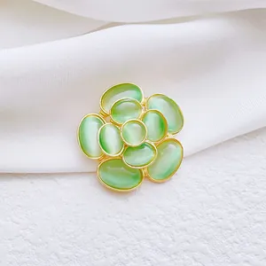 Detalle de broche camelia con piedra de ojo de gato verde y acabado en dorado