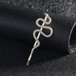 Macro detail of a silver snake bobby pin featuring green gem eyes and textured scales