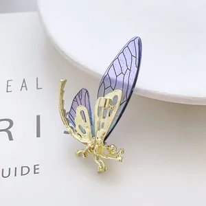 Close-up of golden insect brooch with purple gradient wings and bio-inspired patterns