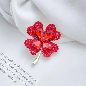 Elegant gold-tone four-leaf clover brooch with red rhinestones on silk fabric