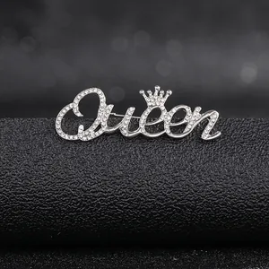 Close-up of a silver Queen letter brooch with rhinestones and a small crown detail