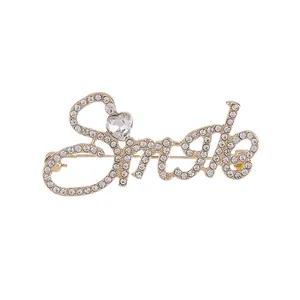 Golden Smile letter brooch with white rhinestones and a heart crystal on white background