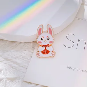 Détail d'une broche en émail de lapin tenant un sac de fortune rouge sur tissu blanc