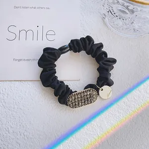 Chouchou élégant en tissu noir avec strass gris étincelants et breloque logo doré