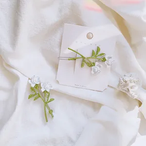 Detail of white 3D rose hair clips with green leaves on a branded card display