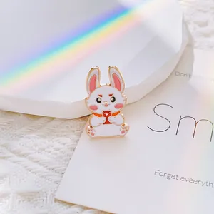 Détail d'une broche lapin en émail blanc avec enveloppe rouge et bordure dorée