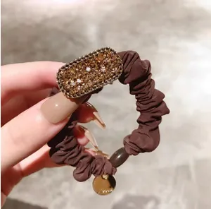 Détail du chouchou marron café avec ornement ovale en strass ambrés et médaille dorée