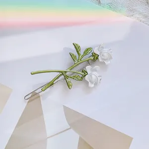 Detailed view of elegant white rose hair clip with green leaves and silver metal base