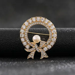 Detalle de broche de corona dorada con strass brillantes y una gran perla central