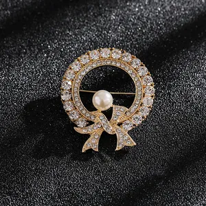 Detalle de un broche de corona dorada con diamantes de imitación y una perla central