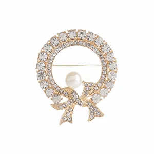 Detalle de broche de corona dorada con perla blanca y cristales de estrás brillantes